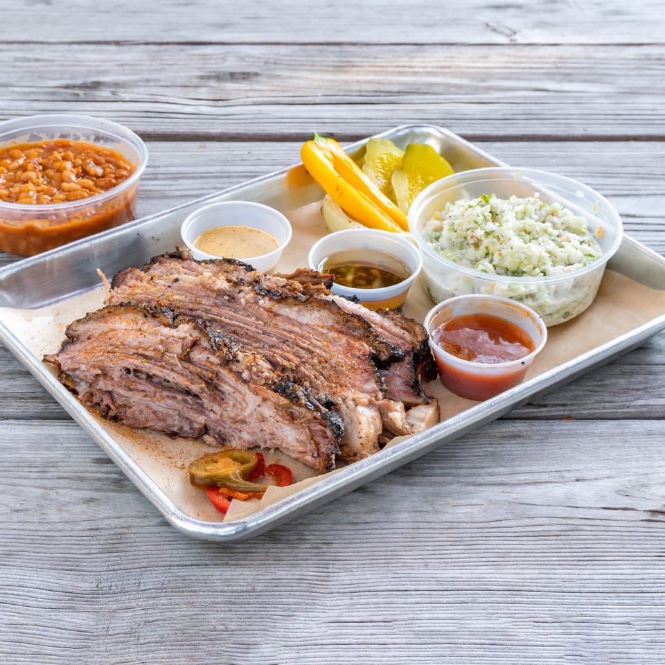 Munchies Live BBQ brisket platter with baked beans, coleslaw, pickles, and sauces on a wooden table.