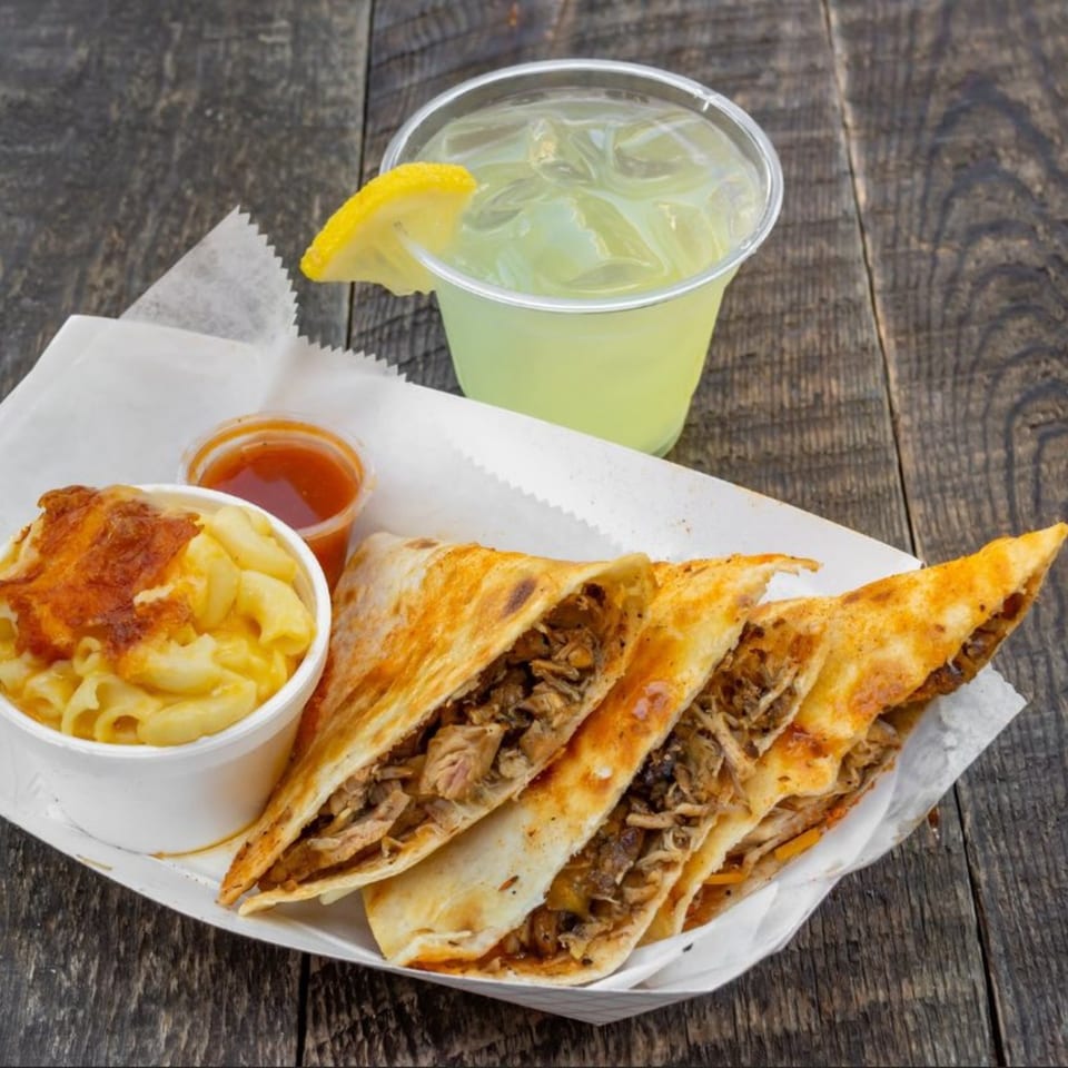 Munchies Live BBQ quesadillas with mac and cheese, sauce, and a lemonade on a wooden table.