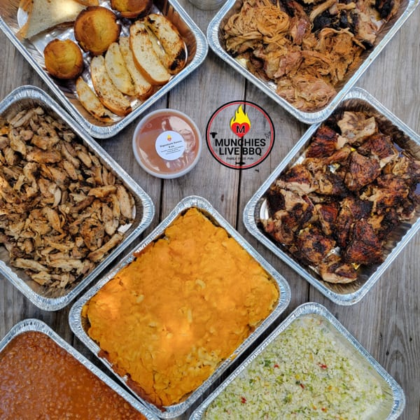 An overhead view of various BBQ dishes in foil trays, including meats, sides, and cornbread.