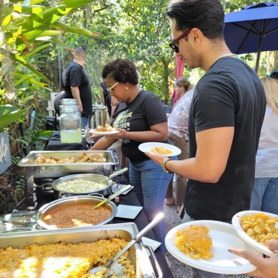 People serving themselves BBQ food from chafing dishes at an outdoor event.