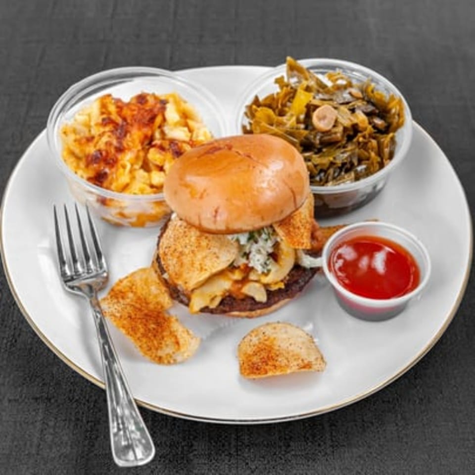 Burger with melted cheese, potato wedges, ketchup, pasta salad, and fries served on a white plate.