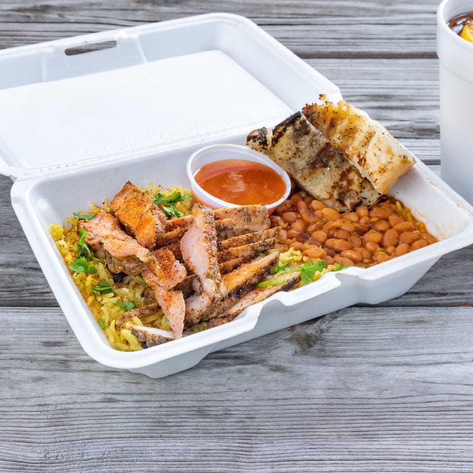 Munchies Live BBQ takeout container with sliced chicken, yellow rice, baked beans, and grilled bread.