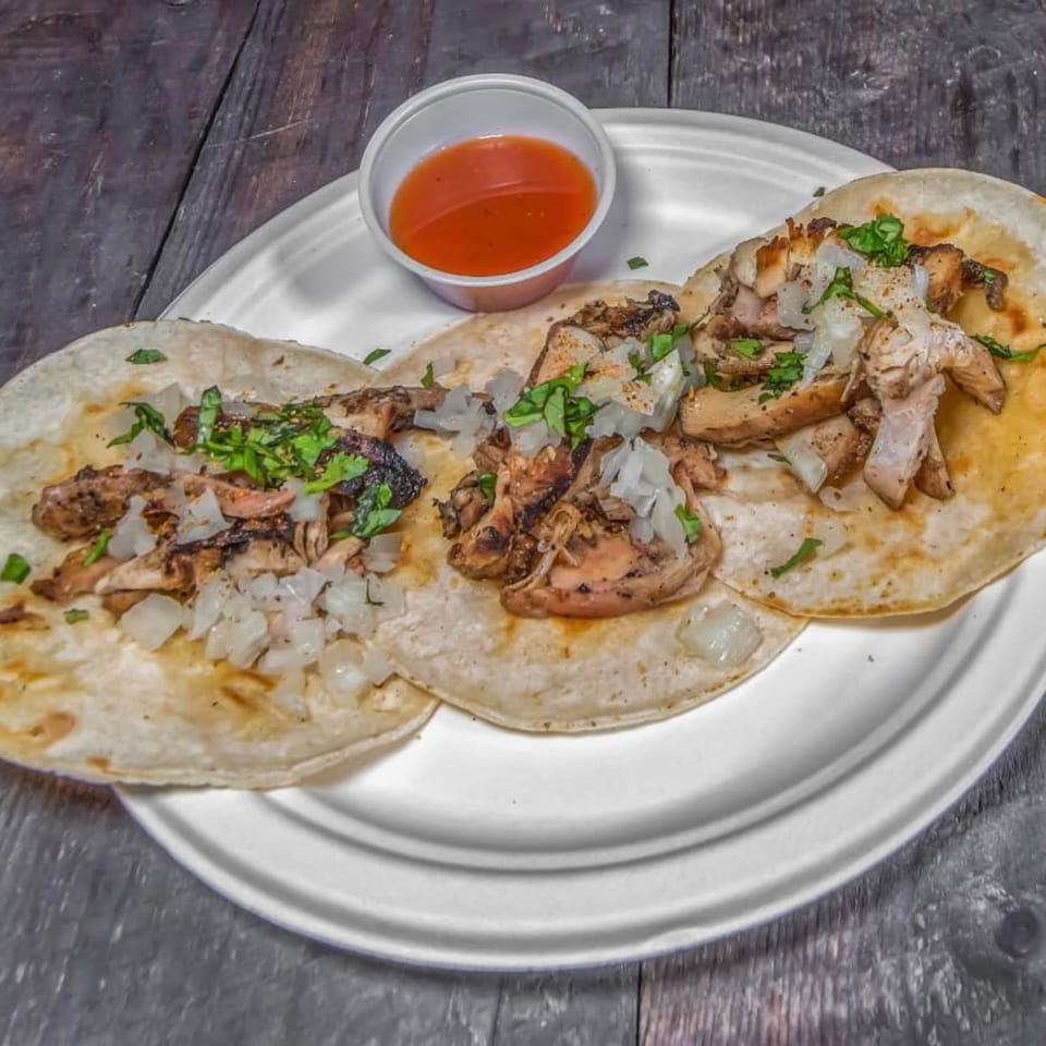 Three BBQ chicken tacos with diced onions and cilantro, served with a side of sauce.